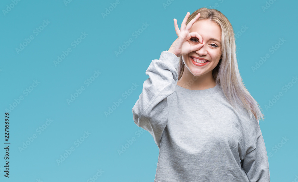 Obraz premium Young blonde woman over isolated background doing ok gesture with hand smiling, eye looking through fingers with happy face.
