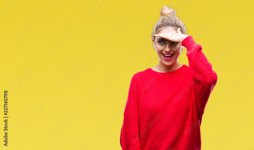 Young beautiful blonde woman wearing red sweater and glasses over isolated background very happy and smiling looking far away with hand over head. Searching concept. Young beautiful blonde woman wearing red sweater and glasses over isolated background very happy and smiling looking far away with hand over head. Searching concept.