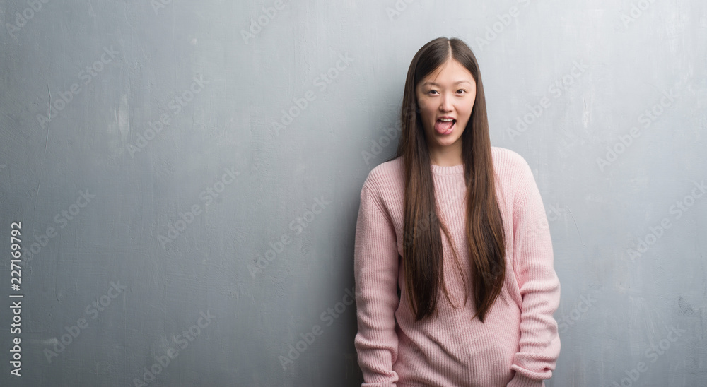 Young Chinese woman over grey wall sticking tongue out happy with funny expression. Emotion concept. Young Chinese woman over grey wall sticking tongue out happy with funny expression. Emotion concept.