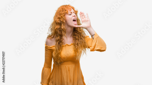 Young redhead woman shouting and screaming loud to side with hand on mouth. Communication concept.