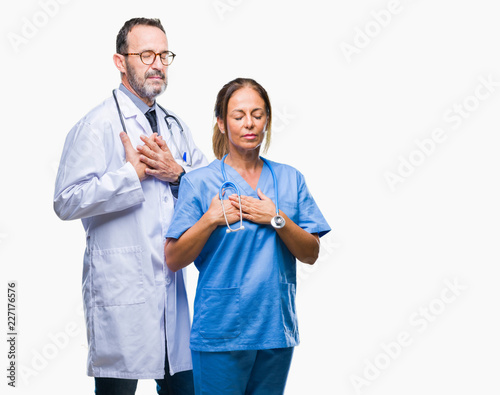 Middle age hispanic doctors partners couple wearing medical uniform over isolated background smiling with hands on chest with closed eyes and grateful gesture on face. Health concept.