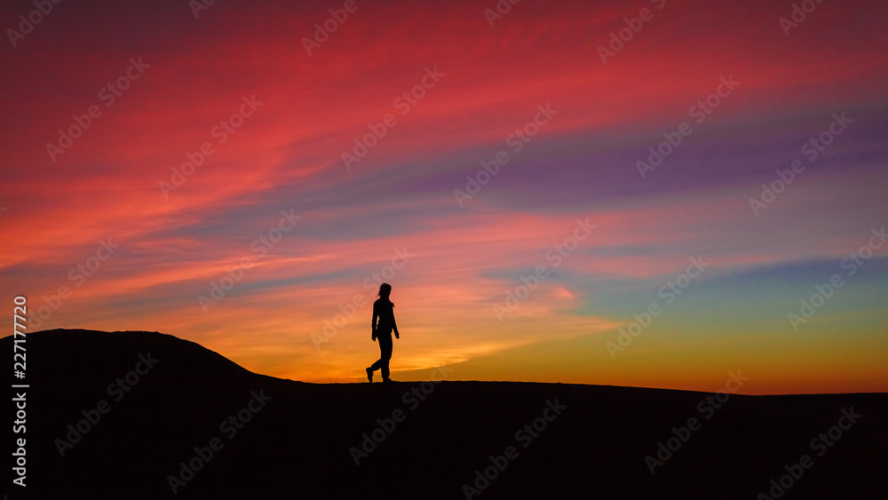 Silhouette of woman walking on sand dune during the sunset