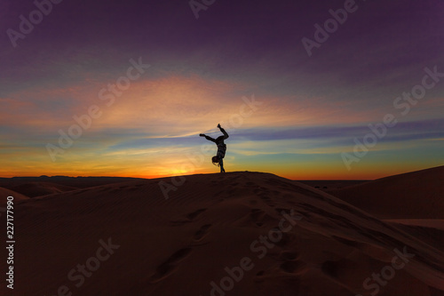 Silhouette of woman doing hand stand on sand dune during the sunset © Boy