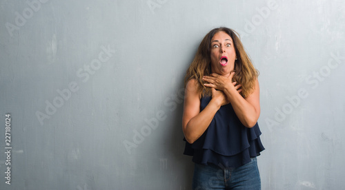 Middle age hispanic woman standing over grey grunge wall shouting and suffocate because painful strangle. Health problem. Asphyxiate and suicide concept.