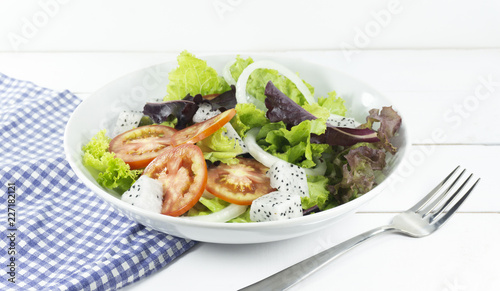Healthy salad diet food concept, props decoration fork and blue Napery, tomatoes Dragon fruit and green and Purple Salad in white Plate on wood floor background, Close up, with copy space.