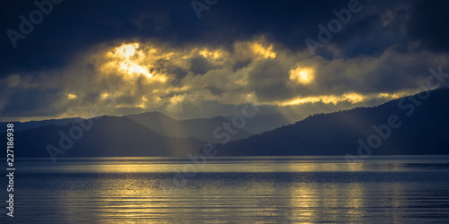 Sun shining through clouds over foggy mountain lake