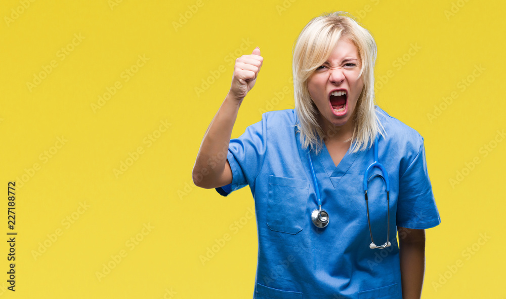 Young beautiful blonde doctor woman wearing medical uniform over isolated background angry and mad raising fist frustrated and furious while shouting with anger. Rage and aggressive concept. Young beautiful blonde doctor woman wearing medical uniform over isolated background angry and mad raising fist frustrated and furious while shouting with anger. Rage and aggressive concept.