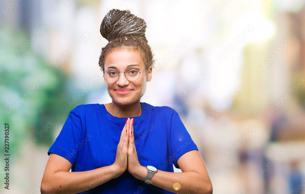 Young braided hair african american girl wearing glasses over isolated background praying with hands together asking for forgiveness smiling confident.
