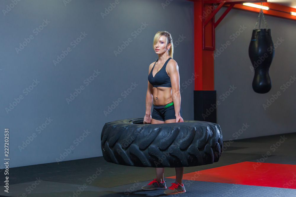 Fit female athlete working out with a huge tire, turning and carry in the  gym. Crossfit woman exercising with big tire Stock Photo | Adobe Stock