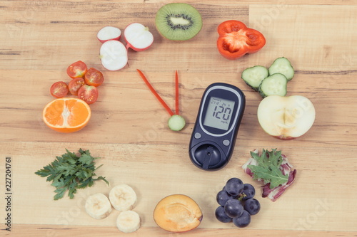 Glucometer with fruits and vegetables showing time of 23 hours 55 minutes, healthy eating for diabetics in new year concept