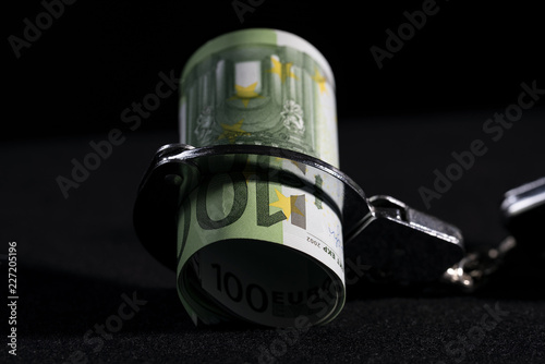 Conceptual image of financial dependence, bundle of money is bound by one side of handcuffs. © igorgeiger