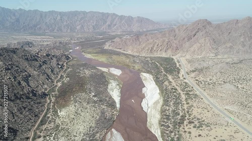 Aerial drone scene with general view of dry rocky mountains and wide Fiambala meandering river landscape. Sand dunes and bus traveling through road. Flying above river at high altitude photo