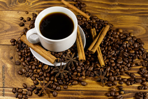 Cup of coffee, roasted coffee beans, star anise and cinnamon sticks on wooden table