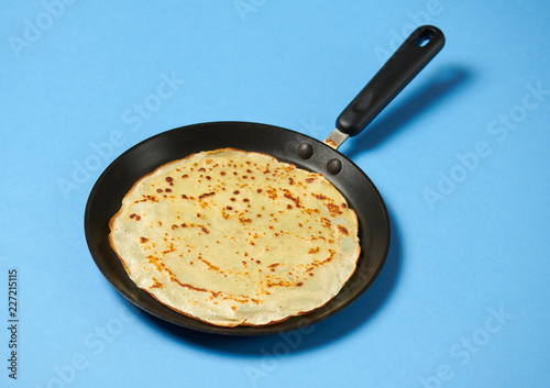 Crepe closeup, thin pancake on a frying pan, blue background