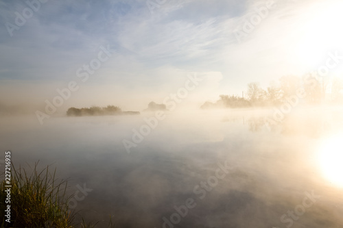 Morning autumn scenery on the bank of the river, wrapped in fog, through which the rays of the sun make their way.