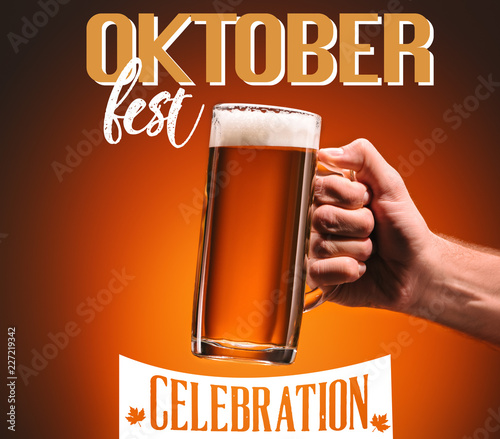 cropped shot of man holding mug of cold beer on orange background with "oktoberfest celebration" lettering