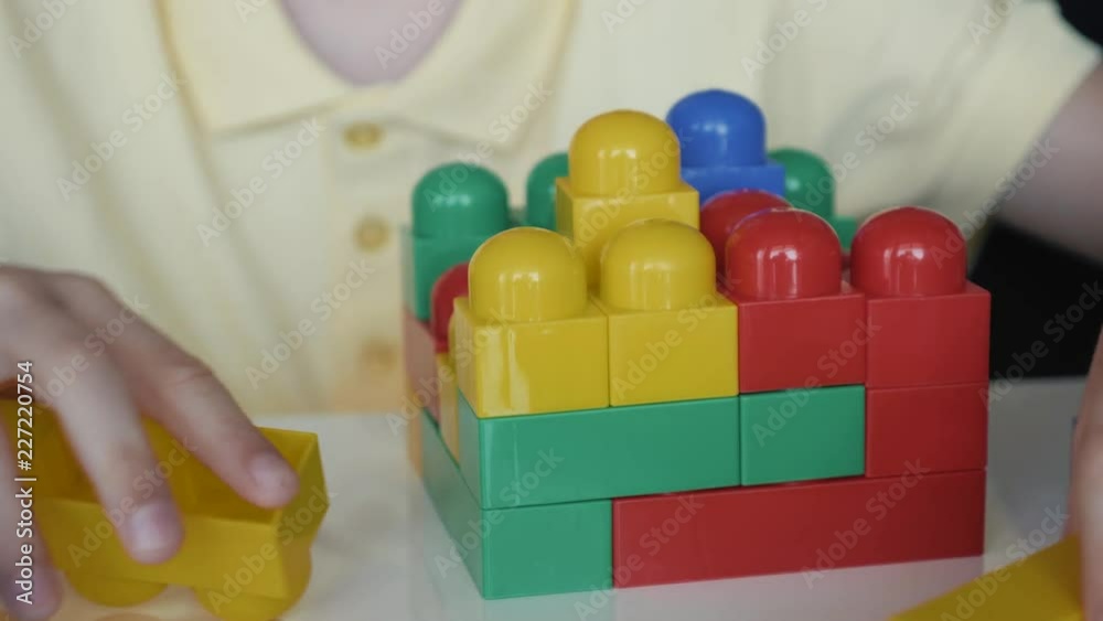 Close-up of the boy's hand collecting the developing designer blocks sitting at the white table. The concept of a happy childhood Close-up of the boy's hand collecting the developing designer blocks sitting at the white table. The concept of a happy childhood