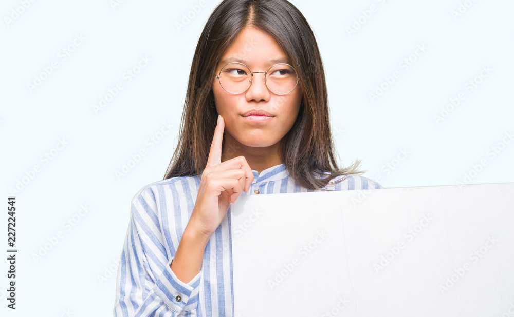 Young asian woman over isolated background holding blank banner serious face thinking about question, very confused idea Young asian woman over isolated background holding blank banner serious face thinking about question, very confused idea