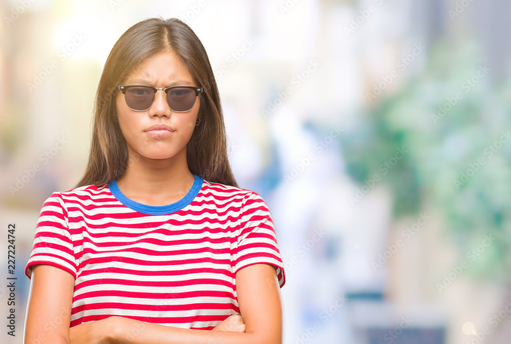 Young asian woman wearing sunglasses over isolated background skeptic and nervous, disapproving expression on face with crossed arms. Negative person.
