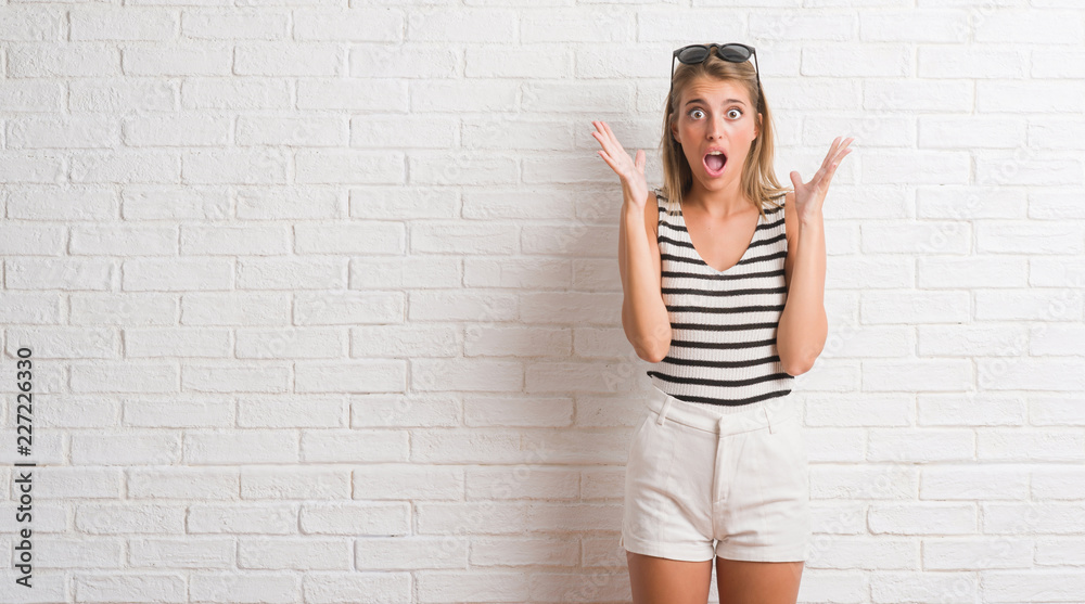 Young beautiful blonde woman over white brick wall celebrating crazy and amazed for success with arms raised and open eyes screaming excited. Winner concept Young beautiful blonde woman over white brick wall celebrating crazy and amazed for success with arms raised and open eyes screaming excited. Winner concept