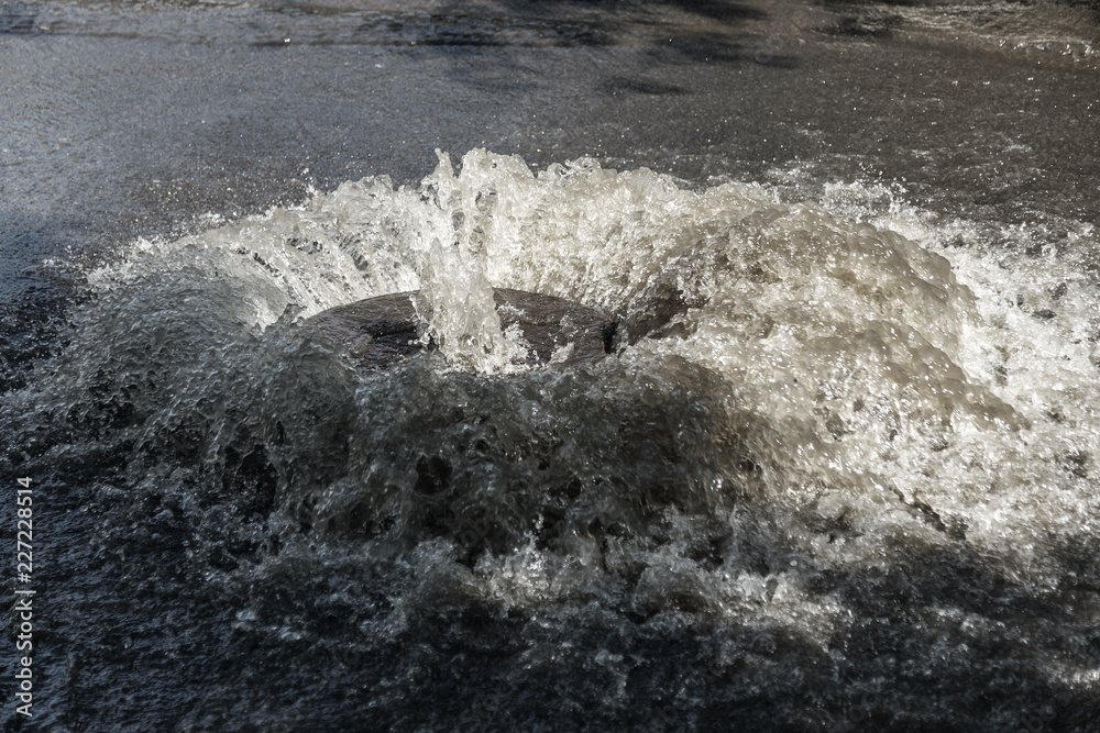 Water flows out of road sewage hatch. Drainage fountain of sewage