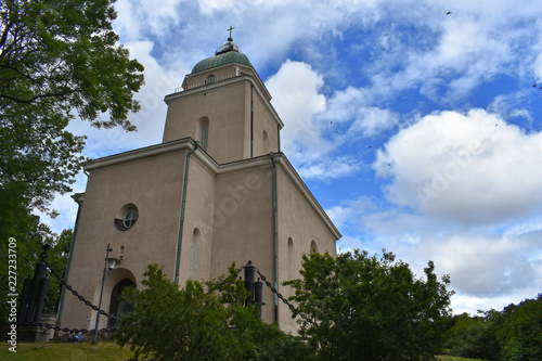 Church with big chain fences and a park full of trees on a cloudy day in the summer time.