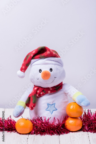 Funny snowman with mandarins and candles on a white wooden background