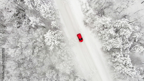 rotes Auto auf einer schneebedeckten eisigen Straße im Winter von oben, Luftbildaufnahme © tronixAS
