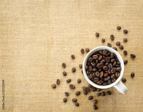 Top view coffee beans in white cup on sackcloth background