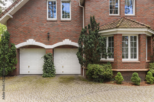 Red brick classic style house with white garage doors and window frames. Cobble in front of the building.