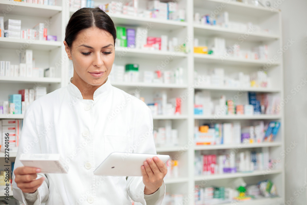 Medicine, pharmaceutics, health care and people concept - Young pharmacist holding a tablet and box of medications.