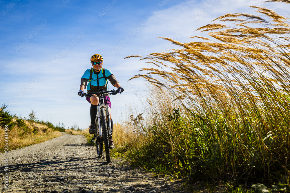 Fototapeta premium Cycling, mountain bikeing woman on cycle trail in autumn forest. Mountain biking in autumn landscape forest. Woman cycling MTB flow uphill trail.