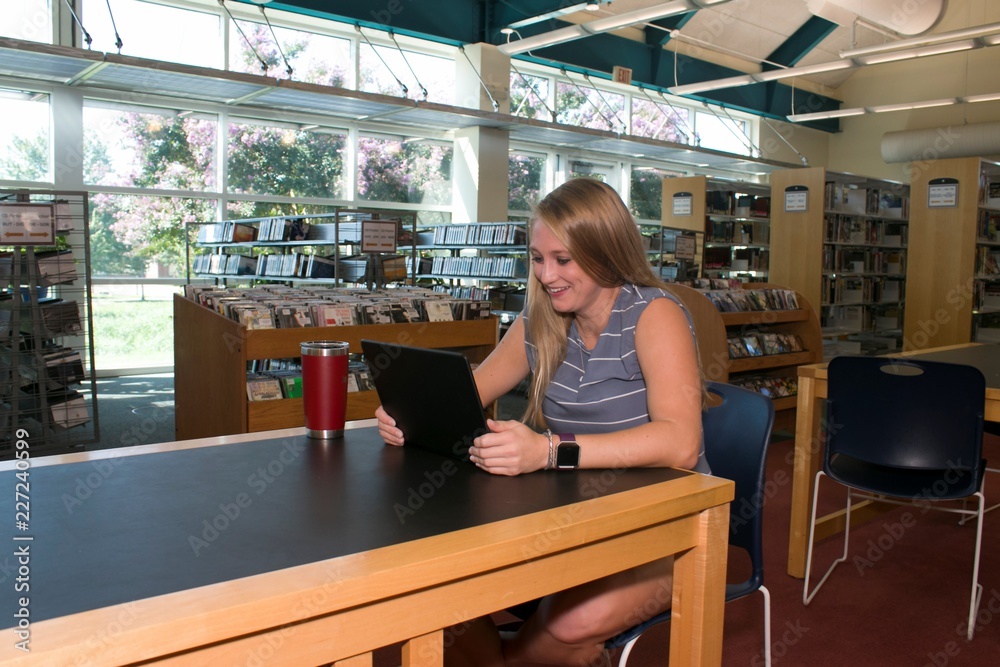 A young woman sips coffee and gazes at her lap top in a library. A young woman sips coffee and gazes at her lap top in a library.