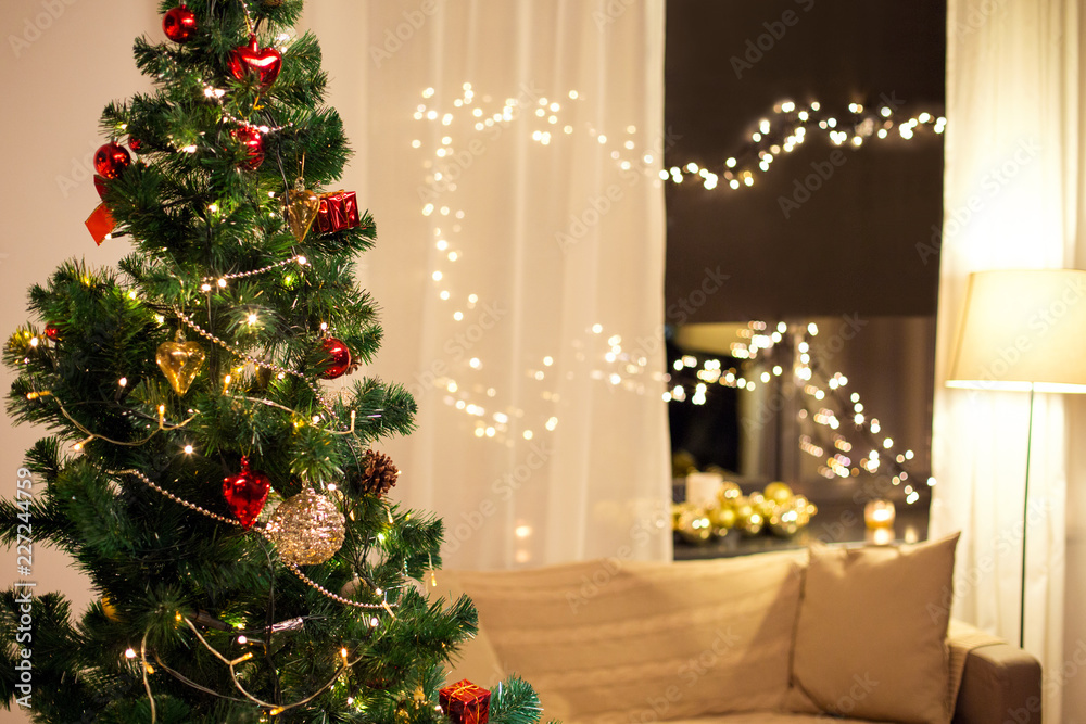 winter holidays and interior concept - close up of decorated christmas tree, sofa and garland on window at home in evening