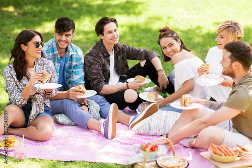 friendship  leisure and fast food concept - group of happy friends eating sandwiches or burgers at picnic in summer park