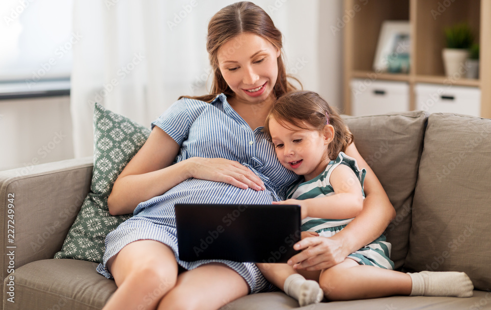 pregnancy, technology and family concept - happy pregnant mother and little daughter with tablet pc computer at home pregnancy, technology and family concept - happy pregnant mother and little daughter with tablet pc computer at home