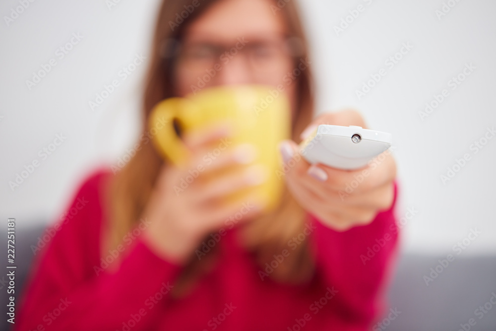Girl holding TV remote and drinking coffee / tea on a couch. Girl holding TV remote and drinking coffee / tea on a couch.