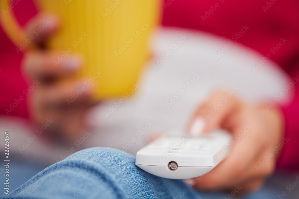 Girl holding TV remote and drinking coffee / tea on a couch. Girl holding TV remote and drinking coffee / tea on a couch.
