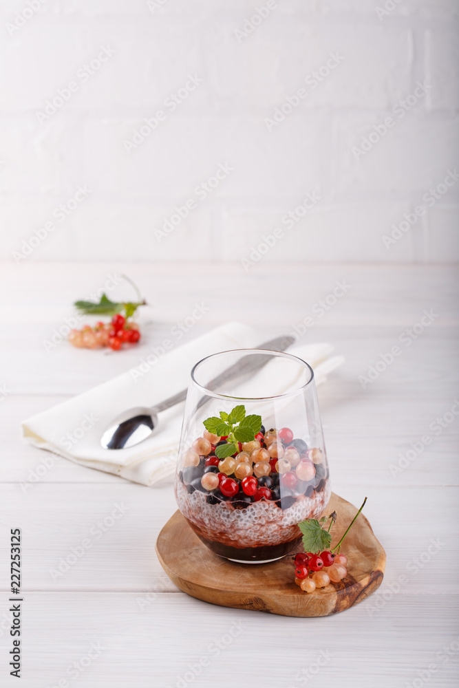 Chia pudding with fresh currant berries in glass on white table.