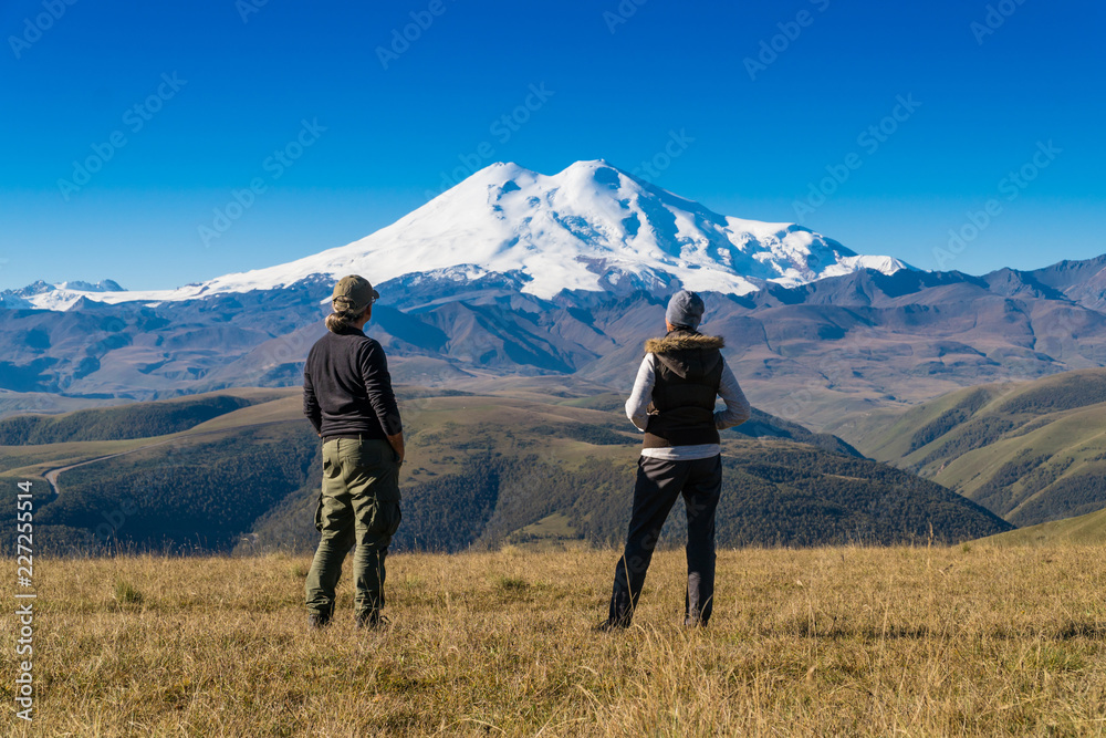 Man and woman with admiring Elbrus mountain view landscape from the cliff edge. Enjoying nature vacation travel adventure at Caucasus mountains.