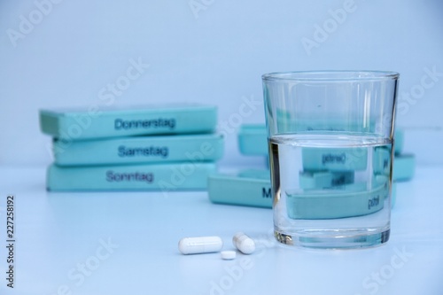 Medikamente, Kapseln, Tabletten und Wasserglas auf einem weißen Tisch