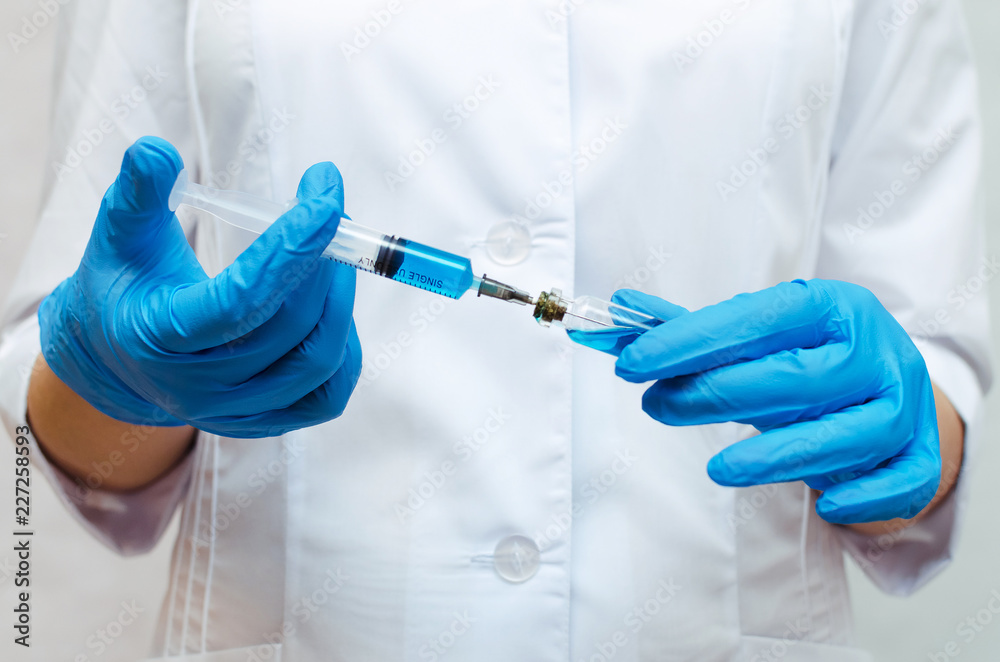 Syringe with a blue medical drug in the doctor hands dressed in the medical gown. Syringe with a blue medical drug in the doctor hands dressed in the medical gown.