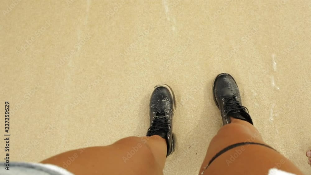Hipster fit girl in sexy shorts and army boots and khaki shirt and travel backpack walk leaving footprints on the beach. Modern tourist active lifestyle. Sport adventure camp on summer vacation.