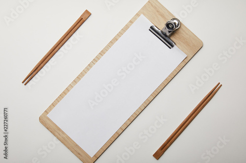 elevated view of arranged blank menu and chopsticks on white surface, minimalistic concept