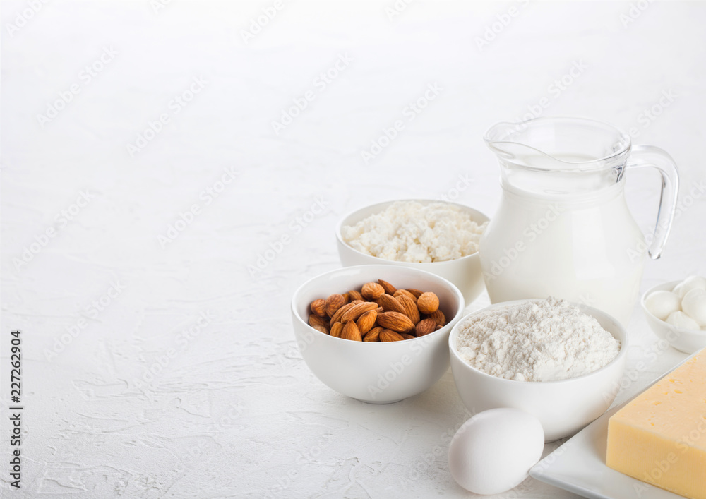 Fresh dairy products on white table background. Glass jar of milk, bowl of cottage cheese and baking flour and almond nuts. Eggs and cheese. Space for text Fresh dairy products on white table background. Glass jar of milk, bowl of cottage cheese and baking flour and almond nuts. Eggs and cheese. Space for text