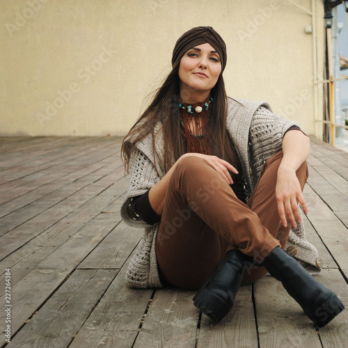 Fashion portrait of a beautiful smiling brunette woman sitting in front of town beach, smiling and looking at camera