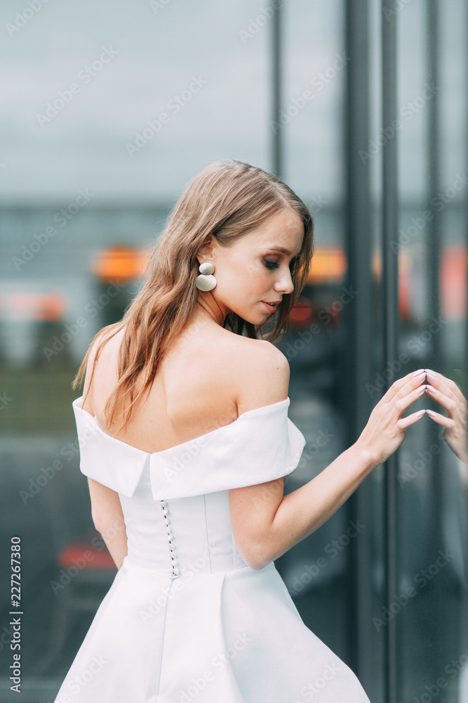 Modern, stylish bride in European dress. Photo shoot on the street near the hotel. Bouquet and strict dress