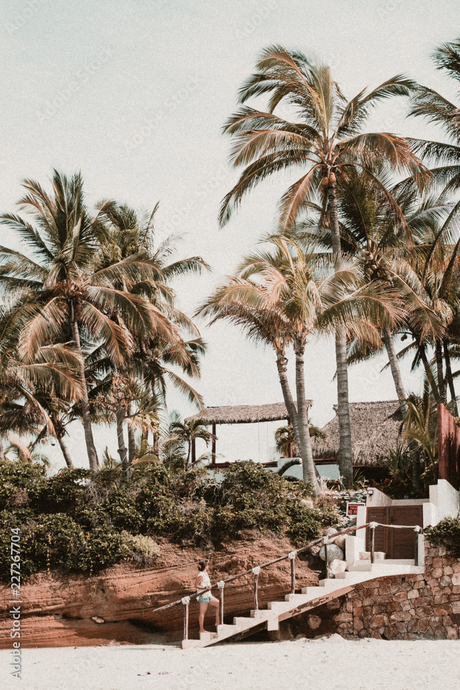 Woman walking up stairs along beach with palm trees