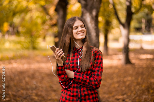 Pretty girl holding phone and listening music with her headphones in autumn