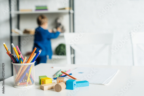 color pencils and wooden blocks on table with album lying on table with little kid blurred on background